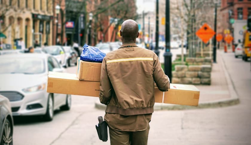 A delivery man walks through the streets of an American city carrying a pile of packages